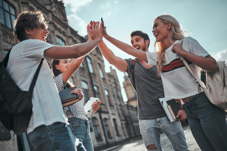 Group of young people are studying together in university. Students outdoors giving five to each other..